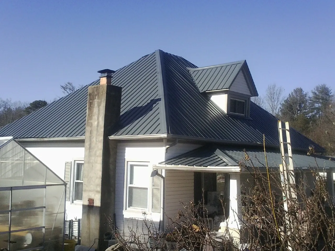Dark blue standing seam metal roof on a white farmhouse with dormer — Slate & Tile Roof Repair by Roofing Brothers in Gibbon