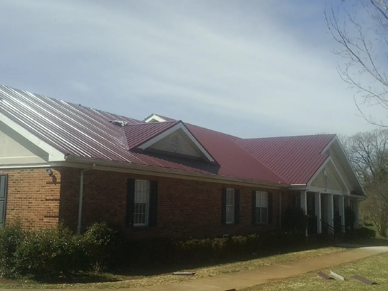 Red metal roof with gabled entries on a long brick building, from a Hail Damage Roof Repair job in Gibbon