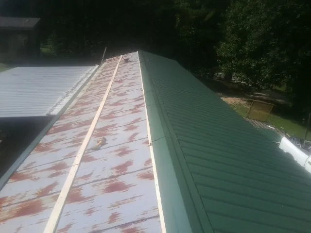Old rusted panels beside newly installed green metal roofing — Wind Damage Roof Repair by Roofing Brothers in Gibbon