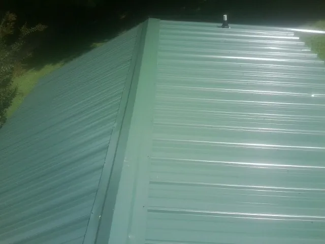 New green metal panels meeting at the ridge of a roof — Flat Roof Repair work by our crew in Gibbon