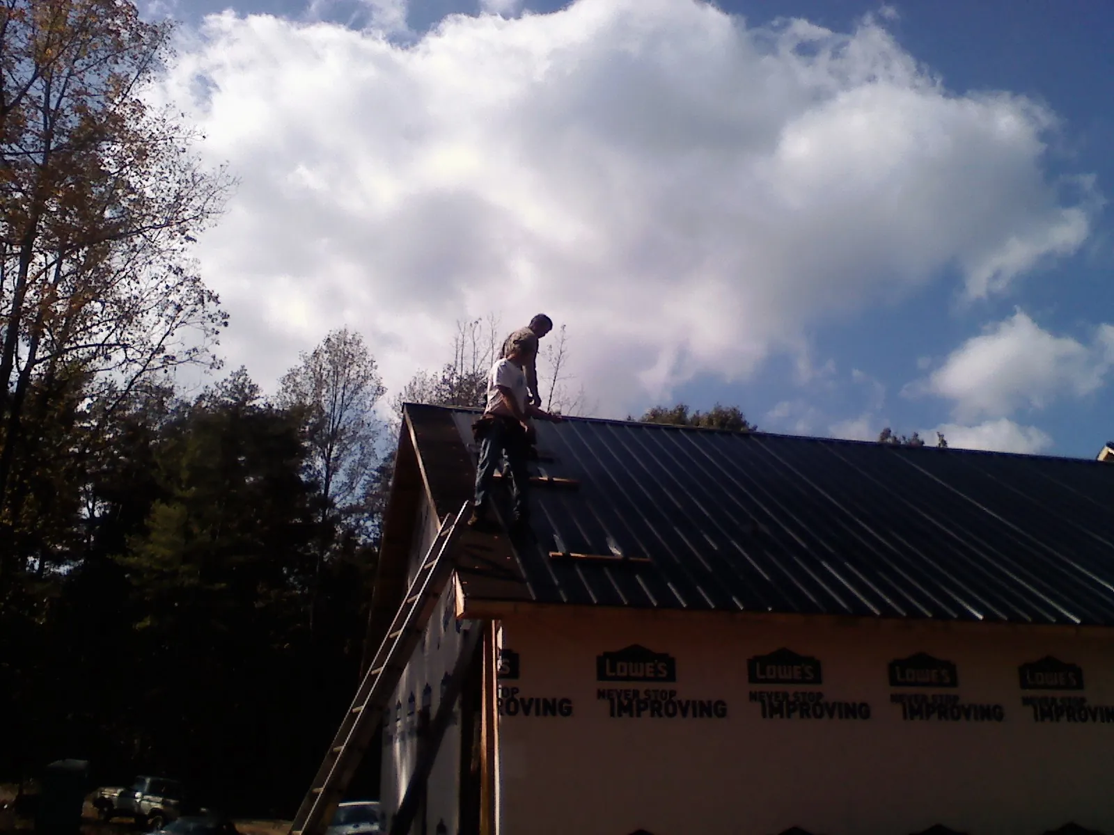 Roofer fastening dark metal panels high against a cloudy sky, from a Roof Inspection job in Gibbon