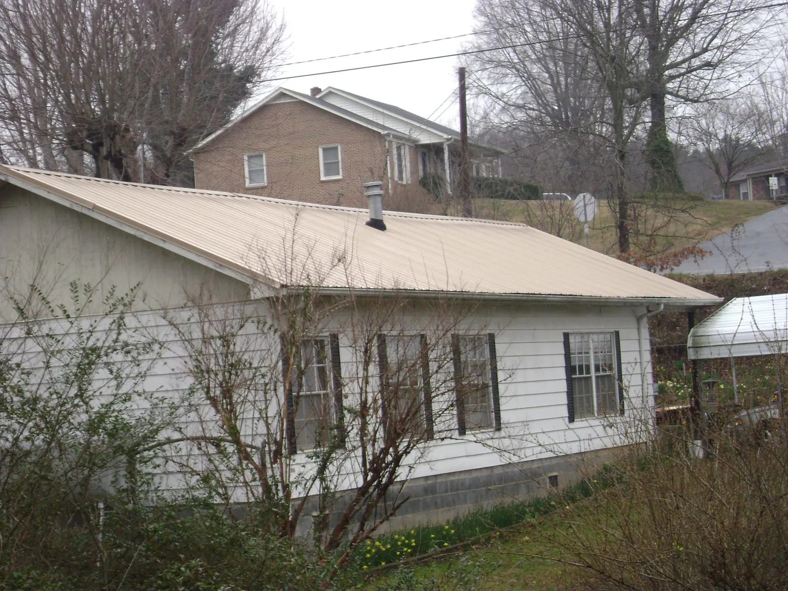 Tan metal roof on a white sided house set into a hillside — Commercial Roofing by Roofing Brothers in Gibbon