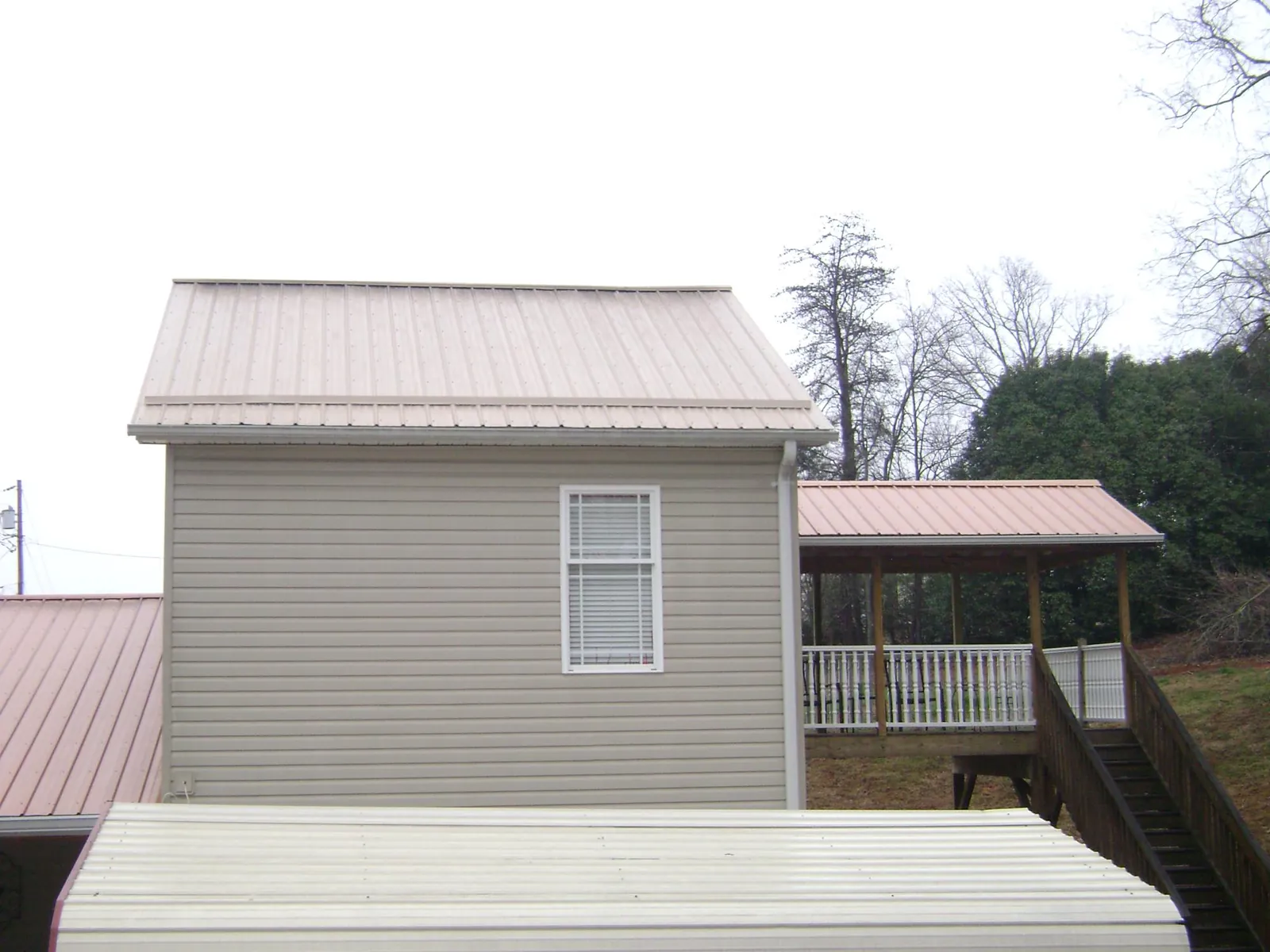 Tan metal roofs on a two story addition and attached porch, from a Roof Replacement job in Gibbon